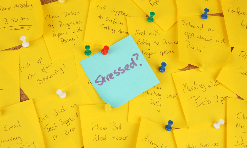 Yellow post its with some tasks like getting snacks written on it with a blue post in the middle that has 'stressed?' written for the office space 